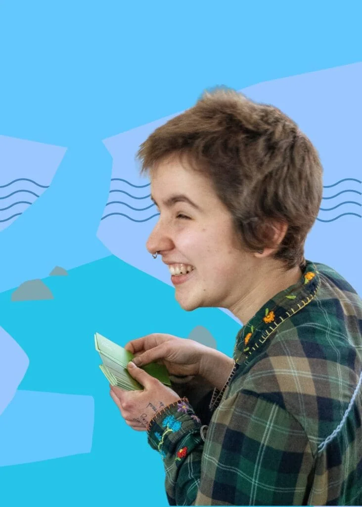 Close up of Caz laughing while holding paint chip on a blue background with waves.