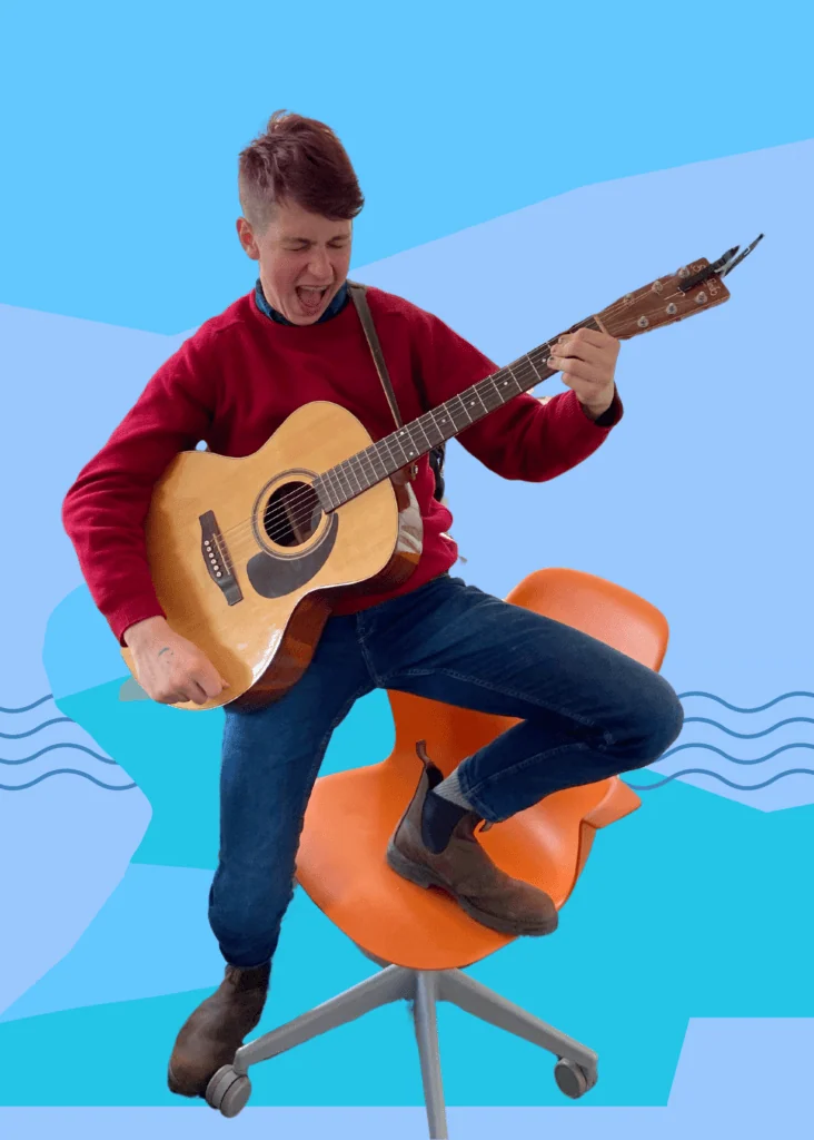 Leo posing with a guitar like a rockstar with one leg up on a chair