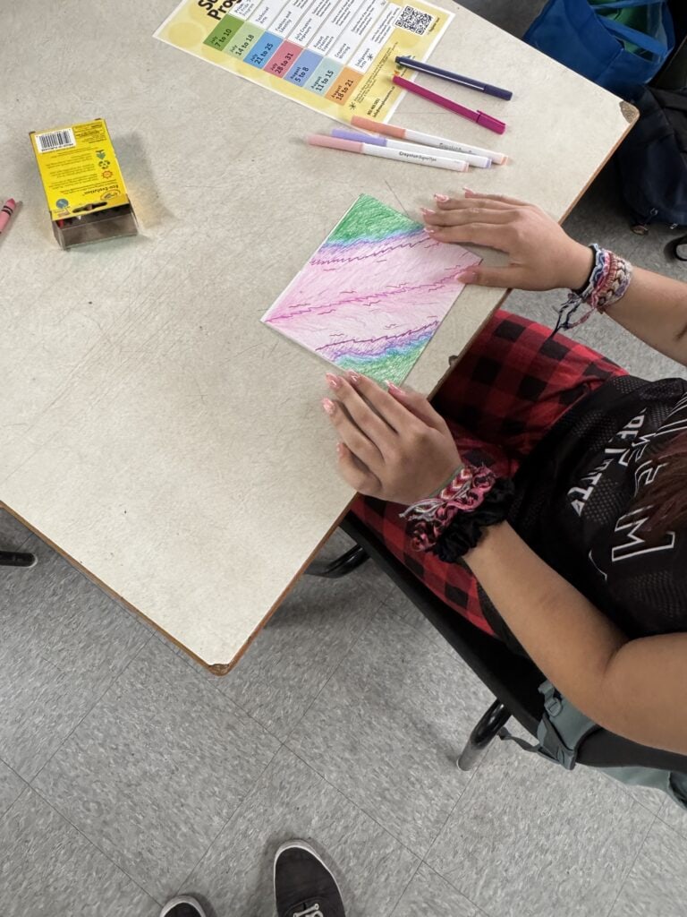 An over the shoulder picture of an individual working on a colourful drawing at a grey table
