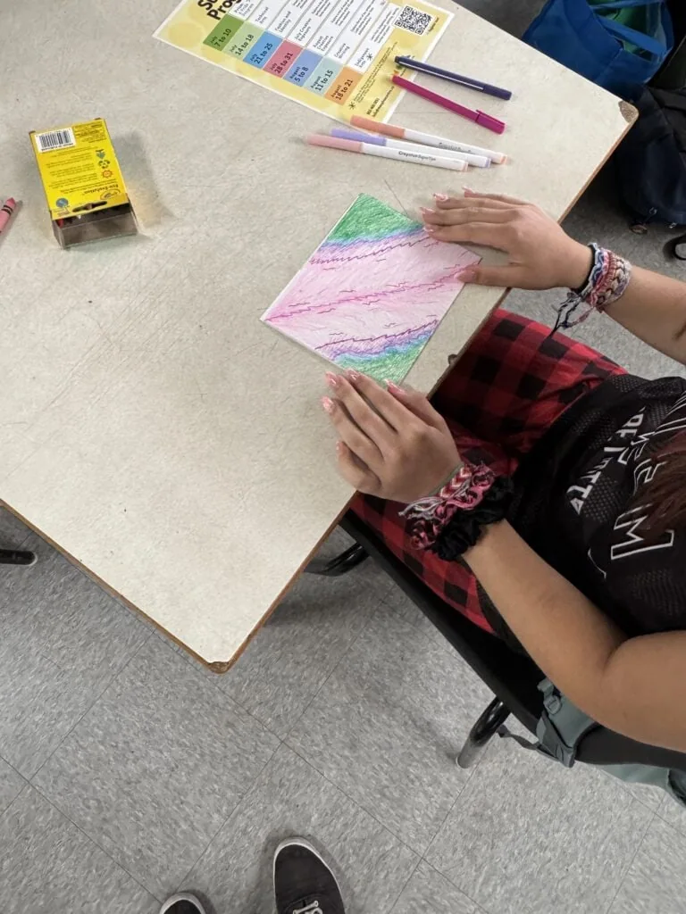 An over the shoulder picture of an individual working on a colourful drawing at a grey table